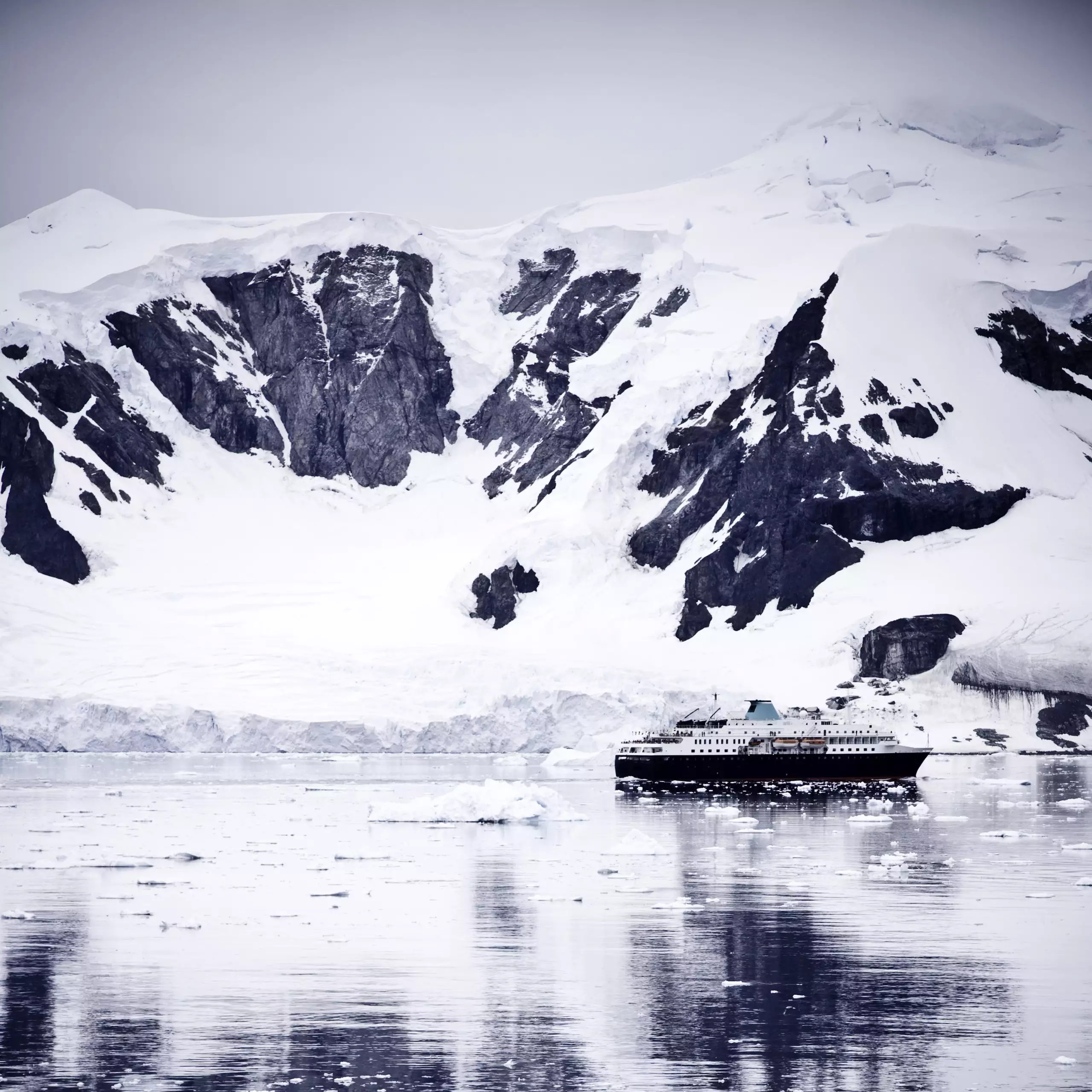 Passagiersschiff vor schneebedeckten Bergen und Eisbergen in der Antarktis, Symbol für Expedition und Traveldesign